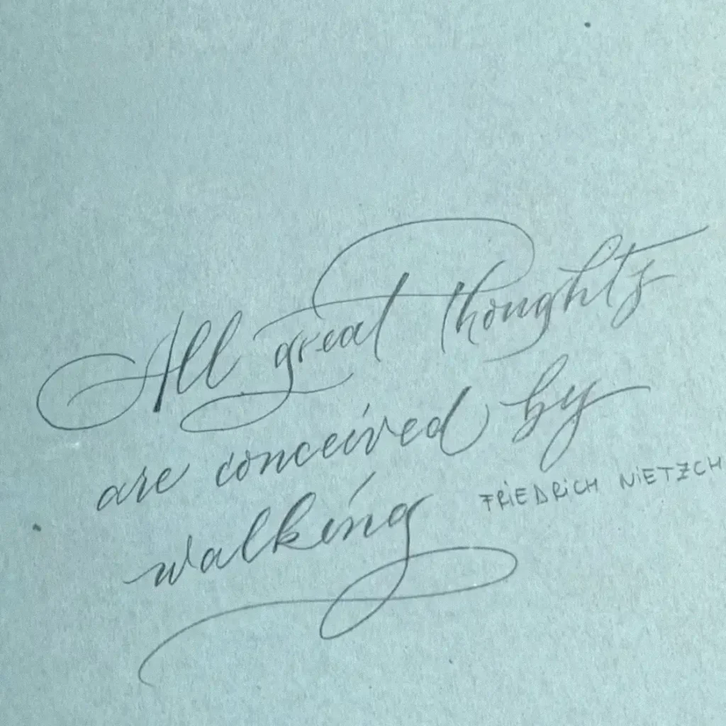 Citatul All great thoughts are conceived by walking de Friedrich Nietzsche caligrafiat meșteșugit pe hârtie albastră