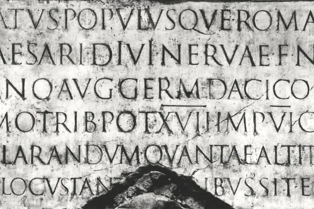 Detaliu al inscripției monumentale cioplite în piatră de la baza Columnelor lui Traian din Roma, scrisă în stilul capitale romane (Capitalis Monumentalis)